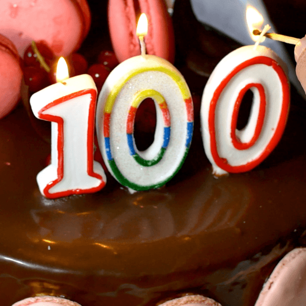 Someone lighting candles on a 100th birthday cake.